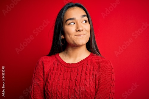 Young beautiful asian woman wearing casual sweater standing over isolated red background smiling looking to the side and staring away thinking.