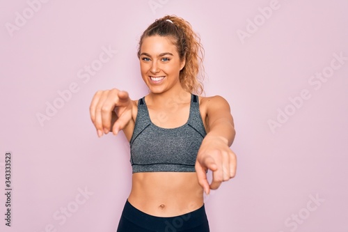 Young beautiful blonde sportswoman with blue eyes doing exercise wearing sportswear pointing to you and the camera with fingers, smiling positive and cheerful
