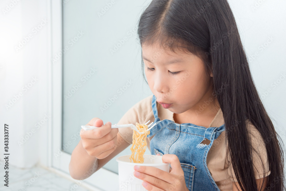 Little asian girl eating instant cup noodle by fork at home. Little asian girl eating instant cup noodle by fork at home.