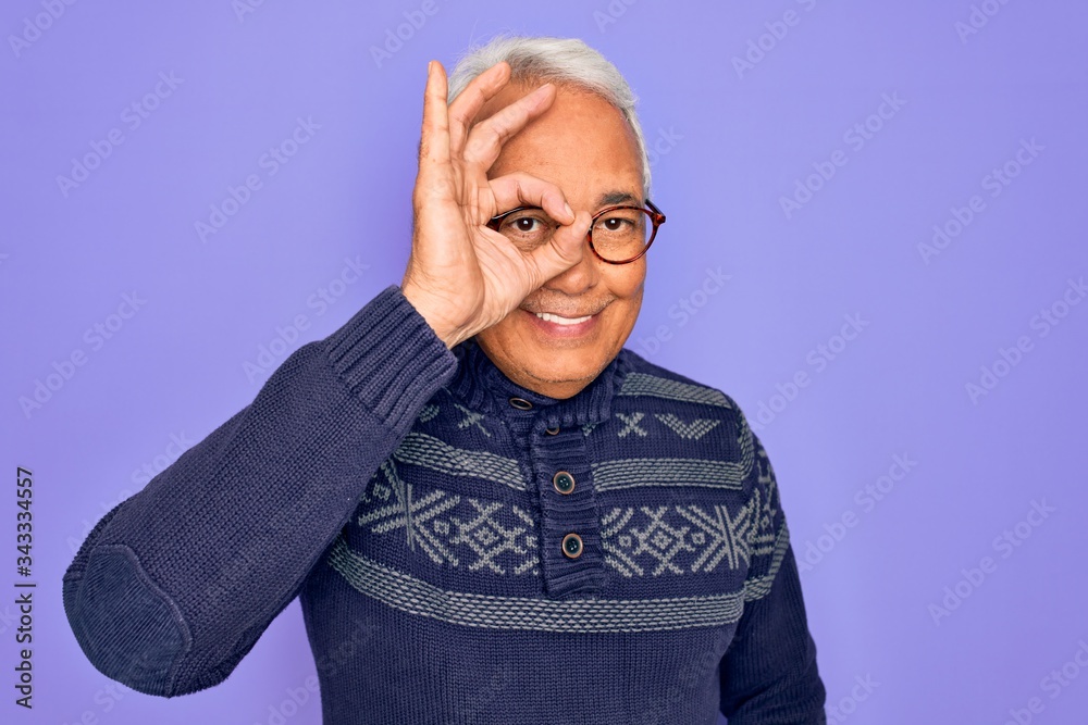 Middle age senior grey-haired man wearing glasses and winter sweater over purple background doing ok gesture with hand smiling, eye looking through fingers with happy face. Middle age senior grey-haired man wearing glasses and winter sweater over purple background doing ok gesture with hand smiling, eye looking through fingers with happy face.