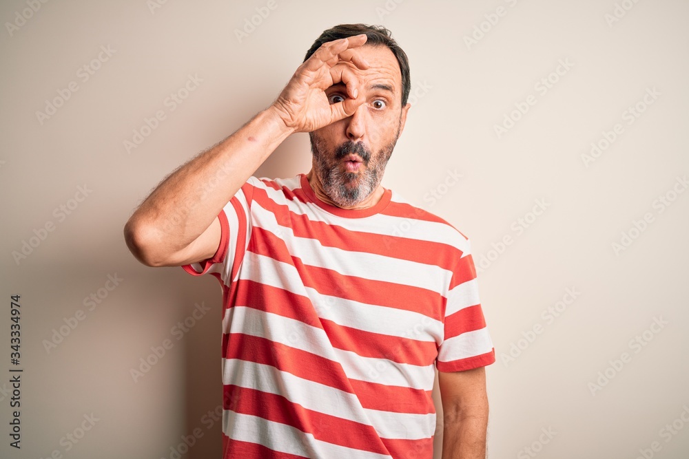 Middle age hoary man wearing casual striped t-shirt standing over isolated white background doing ok gesture shocked with surprised face, eye looking through fingers. Unbelieving expression. Middle age hoary man wearing casual striped t-shirt standing over isolated white background doing ok gesture shocked with surprised face, eye looking through fingers. Unbelieving expression.