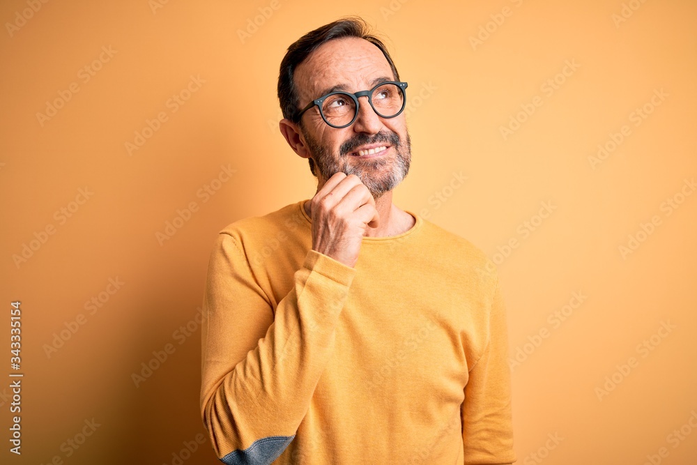 Middle age hoary man wearing casual sweater and glasses over isolated yellow background with hand on chin thinking about question, pensive expression. Smiling and thoughtful face. Doubt concept. Middle age hoary man wearing casual sweater and glasses over isolated yellow background with hand on chin thinking about question, pensive expression. Smiling and thoughtful face. Doubt concept.