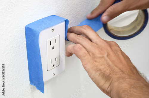 Painter Man Using Masking Blue Tape to Secure Electric Outlet.