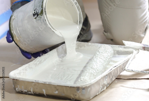 Professional interior construction worker pouring white color paint to tray.