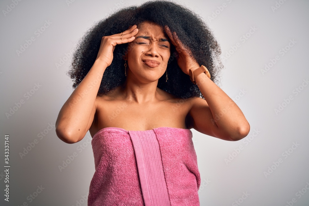 Young african american woman with afro hair wearing a body towel after beauty care shower suffering from headache desperate and stressed because pain and migraine. Hands on head. Young african american woman with afro hair wearing a body towel after beauty care shower suffering from headache desperate and stressed because pain and migraine. Hands on head.