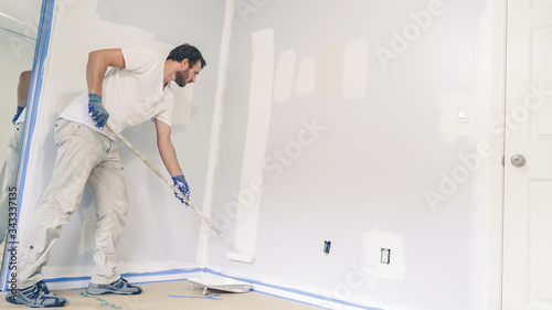 Painter man painting the wall in home, with paint roller and white color paint.