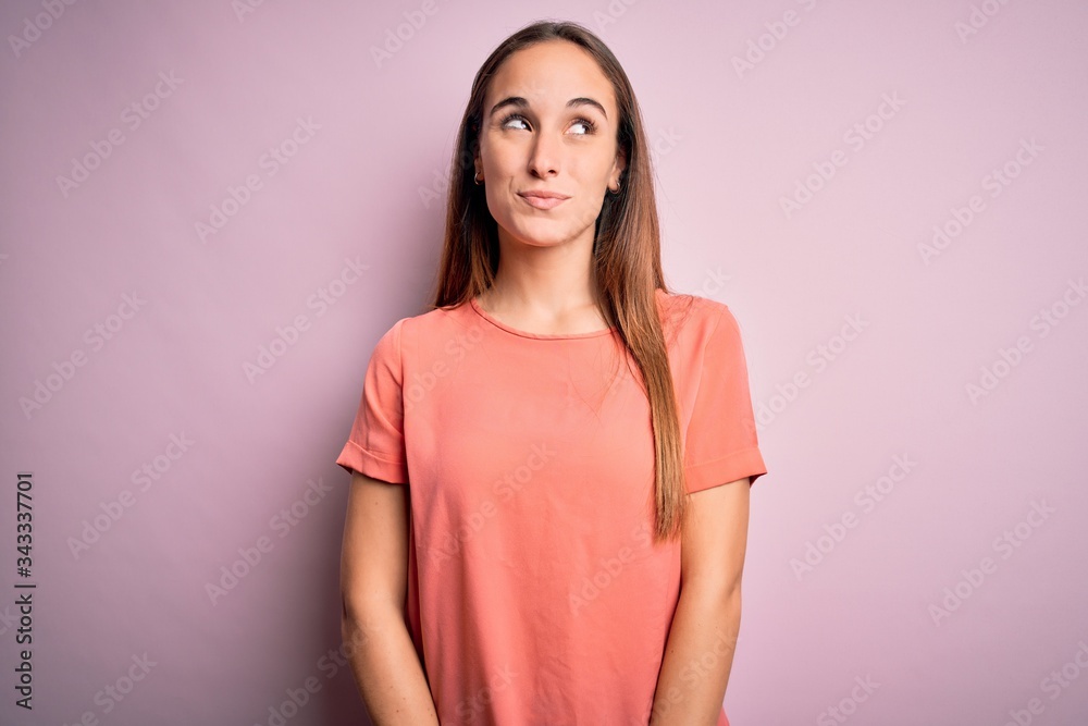 Young beautiful woman wearing casual t-shirt standing over isolated pink background smiling looking to the side and staring away thinking. Young beautiful woman wearing casual t-shirt standing over isolated pink background smiling looking to the side and staring away thinking.