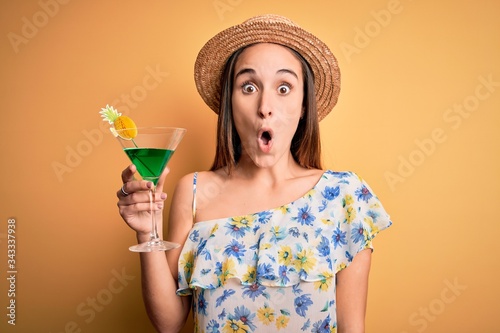 Young beautiful tourist woman on vacation wearing summer hat drinking cocktail beverage scared in shock with a surprise face, afraid and excited with fear expression