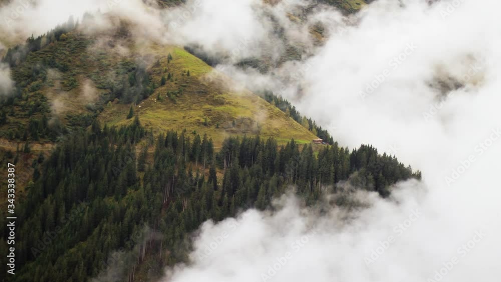 Zoom in timelapse showing scattered low hanging clouds surrounding a distant remote hut in the forest-covered mountains. Zoom in timelapse showing scattered low hanging clouds surrounding a distant remote hut in the forest-covered mountains.