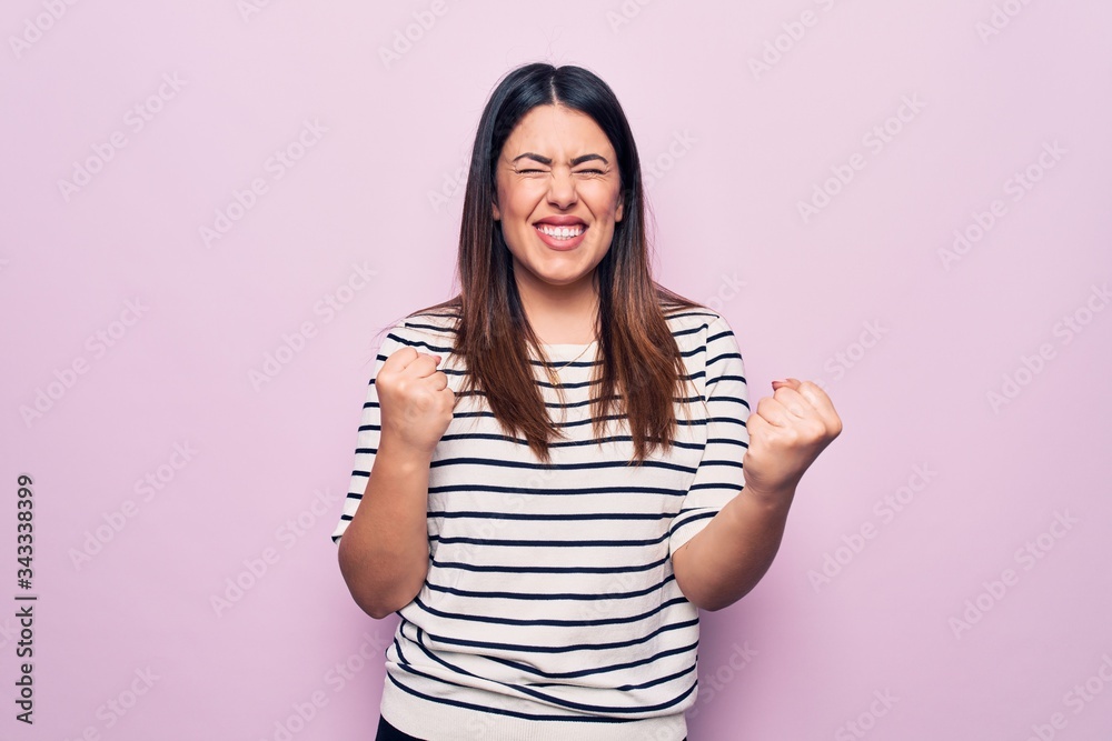 Young beautiful brunette woman wearing casual striped t-shirt over isolated pink background celebrating surprised and amazed for success with arms raised and eyes closed