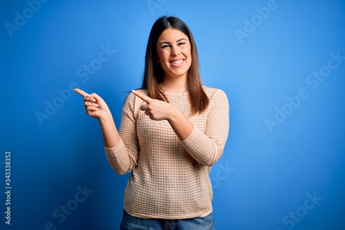Young beautiful woman wearing casual sweater over blue background smiling and looking at the camera pointing with two hands and fingers to the side.