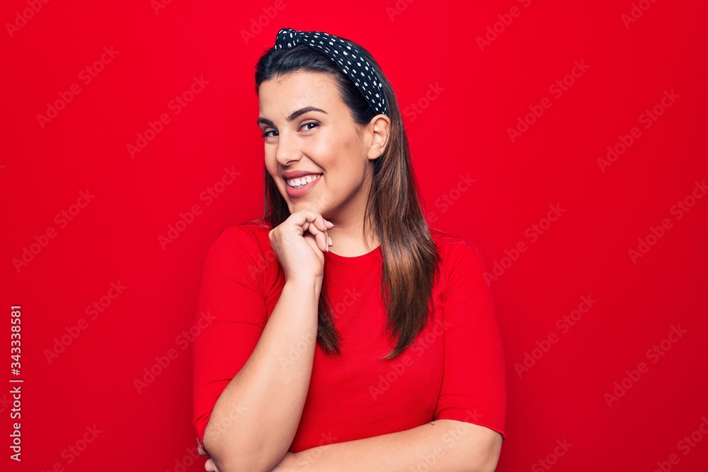 Young beautiful brunette woman wearing casual t-shirt standing over isolated red background smiling looking confident at the camera with crossed arms and hand on chin. Thinking positive. Young beautiful brunette woman wearing casual t-shirt standing over isolated red background smiling looking confident at the camera with crossed arms and hand on chin. Thinking positive.