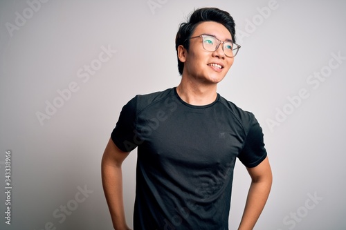 Young handsome chinese man wearing black t-shirt and glasses over white background looking away to side with smile on face, natural expression. Laughing confident. © Krakenimages.com