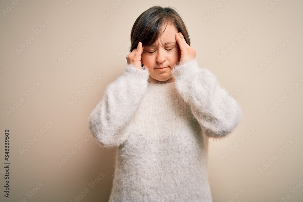 Young down syndrome woman standing over isolated background with hand on head for pain in head because stress. Suffering migraine. Young down syndrome woman standing over isolated background with hand on head for pain in head because stress. Suffering migraine.