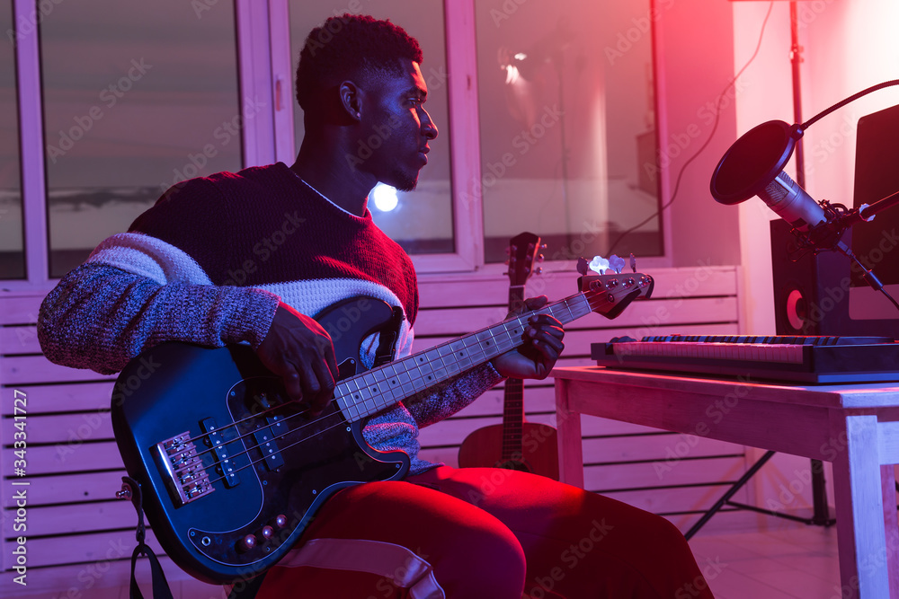 Fototapeta Create music and a recording studio concept - African american man guitarist recording electric bass guitar track in home studio