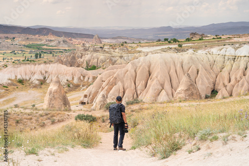 A man with backpack walking on mountain trail looking to Goreme town in Capadocia plateau, central Anatolia in Turkey