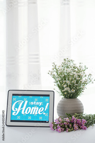 Stay home advice on tablet computer and vase with blooming wild flowers