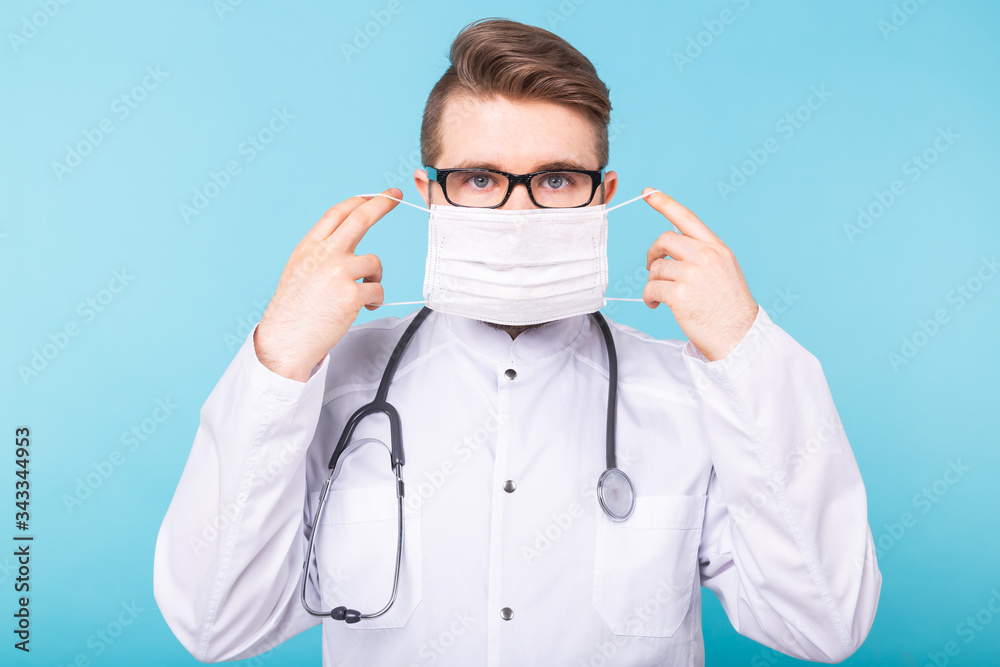 Man doctor puts on medical mask on blue background. Coronavirus, covid-19 and pandemic concept. Man doctor puts on medical mask on blue background. Coronavirus, covid-19 and pandemic concept.