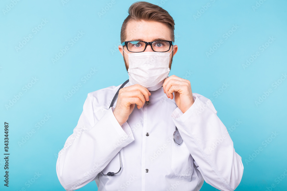 Man doctor puts on medical mask on blue background. Coronavirus, covid-19 and pandemic concept.