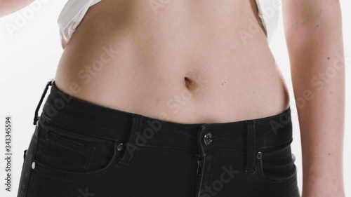 Close-up of a woman's stomach as she holds up her shirt to show off her slim waist.
