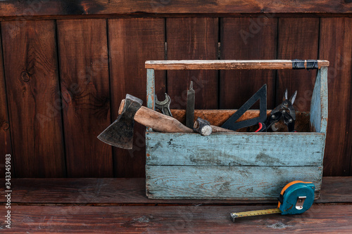 A blue old wooden tool box with an axe, hammer, tape measure and other tools in a wooden room. Space for text, copy space