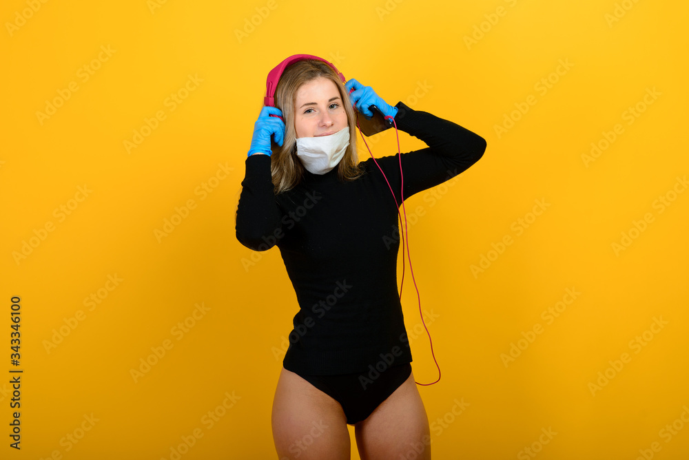 Portrait of a girl in a medical mask, which puts on a rubber glove. Yellow and grey background. Copy space. Portrait of a girl in a medical mask, which puts on a rubber glove. Yellow and grey background. Copy space.