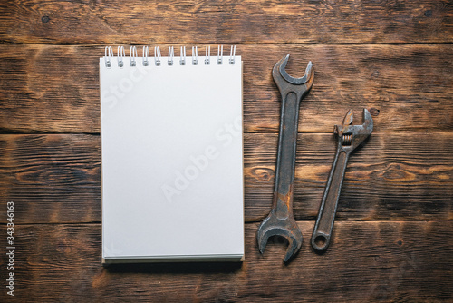 Old wrenches and blank page notepad on brown wooden workbench background. Fix list.