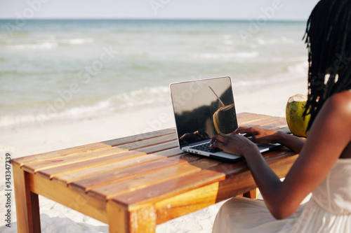 Female freelancer or blogger sitting at table on the beautiful beach and working on laptop photo