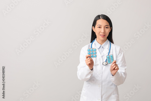 Female Asian doctor with pills on light background