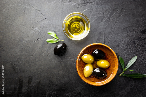 Black and green olives and olive oil in wooden bowls on black background. Top view with copy space for text.