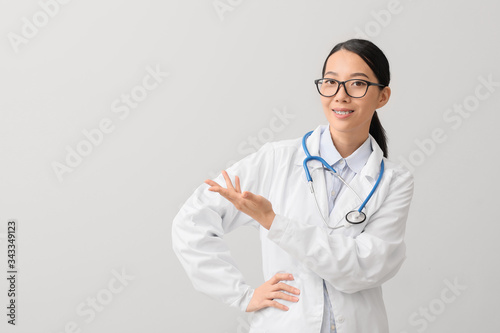 Female Asian doctor showing something on light background
