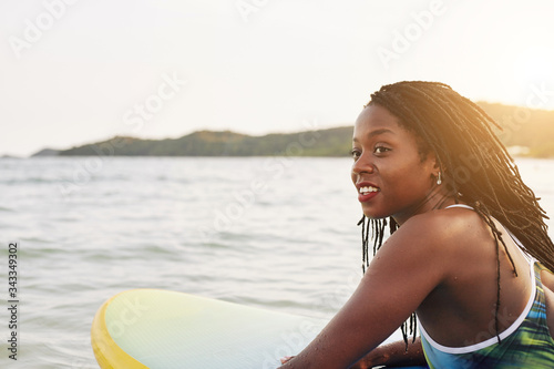 Beautiful smiling young Black woman sub surfing in ocean under rays of sunset sun photo