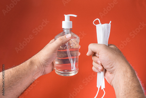Man hand in container with alcohol gel and surgical mask on the red background © Mateus
