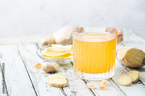 Yellow drink with ginger, lemon and ice in a glass, refreshing homemade ginger lemonade or ale on white background