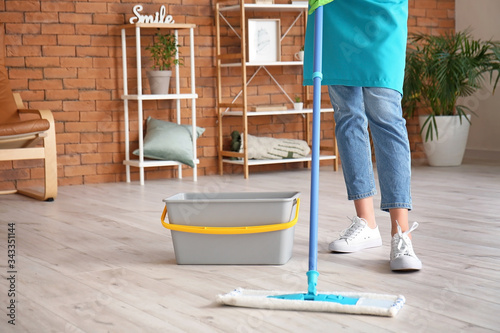 Young woman mopping floor in room