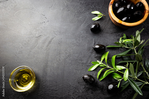 Black olives and olive oil in wooden bowls on black background. Top view with copy space for text.