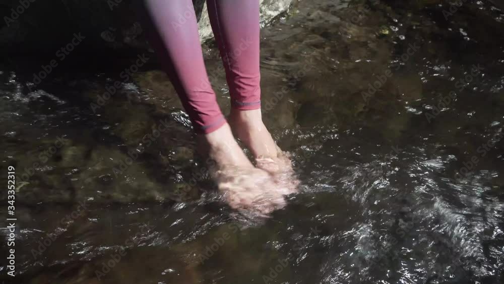 Close up, young woman puts legs in the water of a small river.It`s summer, cooling her white skin feets in fresh water. Playing with the water, splashing around Close up, young woman puts legs in the water of a small river.It`s summer, cooling her white skin feets in fresh water. Playing with the water, splashing around