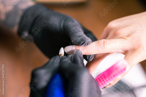 Female master uses an electric machine to remove the nail polish during manicure in the salon. Close-up hardware manicure. Concept of hand care. Female manicurist cleaning of nails by a milling cutter