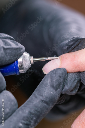 Close-up shot of hardware manicure in a beauty salon. Manicurist is applying electric nail file drill to manicure on female fingers.
