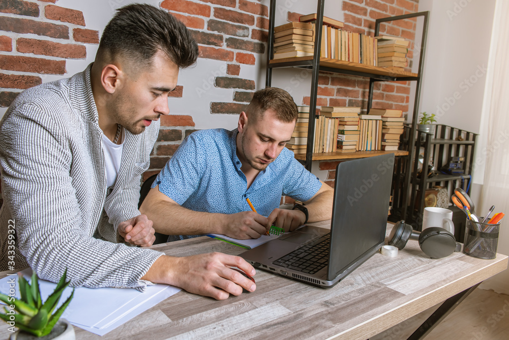 two young men, business people working remotely in the office, sitting at a desk, working with documents, discussing work, emotionally, thinking, tired after work and from work