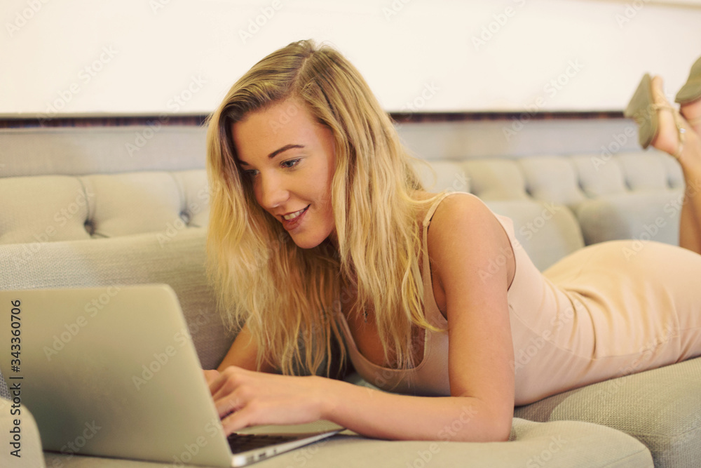 a young smiling businesswoman is working on a laptop lying on a sofa relaxing on holiday a young smiling businesswoman is working on a laptop lying on a sofa relaxing on holiday