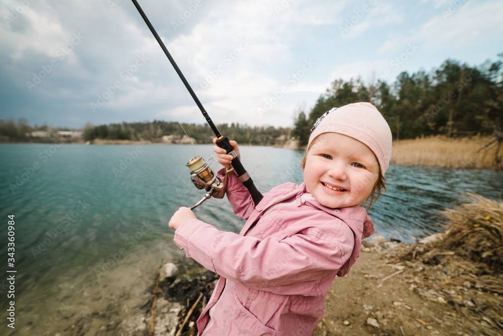 Little girl catching a fish. Lonely happy little child fishing from beach lake or pond with text space. Photo of children pulling rod while fishing on the weekend.