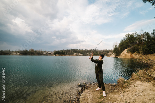 Fisherman with rod throws bait into the water on river bank. Fishing for pike  perch. Background wild nature. The concept of rural getaway. Woman catching a fish on lake or pond with text space.