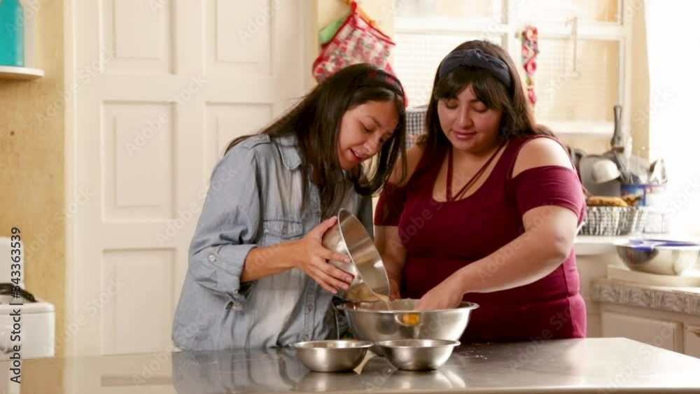 Hispanic sisters mixing ingredients to make homemade cookies - young women cooking at home - activities at home Hispanic sisters mixing ingredients to make homemade cookies - young women cooking at home - activities at home