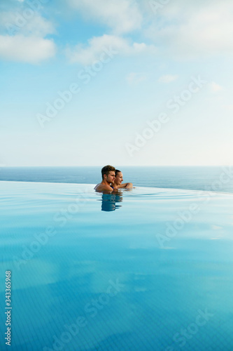 Couple In Love At Luxury Resort On Romantic Summer Vacation. People Relaxing Together In Edge Swimming Pool Water  Enjoying Beautiful Sea View. Happy Lovers On Honeymoon Travel. Relationship  Romance