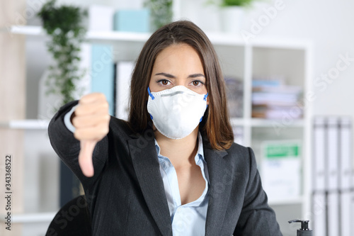Executive with mask gesturing thumbs down looking camera