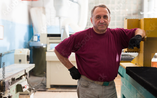 Portrait of elderly foreman in protective gloves standing in workshop