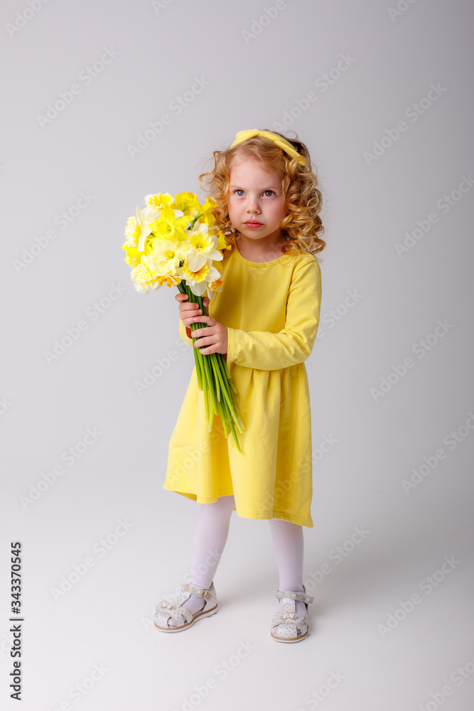 a small curly haired girl in a yellow dress holding a bouquet of spring flowers on a white background smiles a small curly haired girl in a yellow dress holding a bouquet of spring flowers on a white background smiles