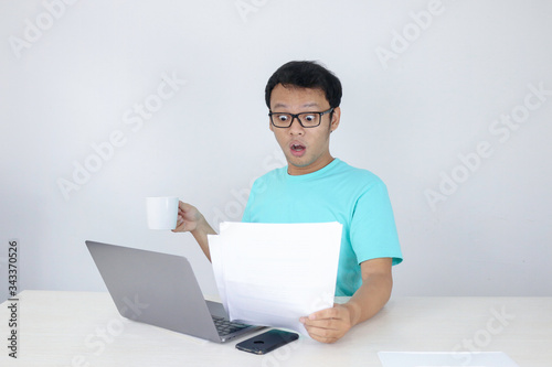 Wow face of Young Asian man shocked what he see in the document when working with laptop. isolated grey background wearing blue shirt.