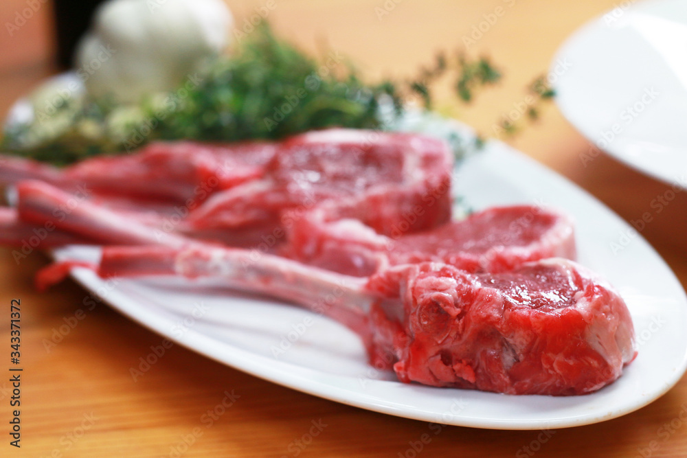Close up image of Raw beef bone rib-eye steak on a plate with onion, garlic and garnish ready to cook on a wooden table.
